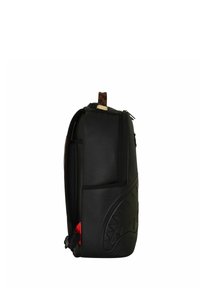 Mochila negra con diseño de cara de tiburón en relieve en el lateral, asa marrón a cuadros y detalle de tela roja cerca de la correa inferior.