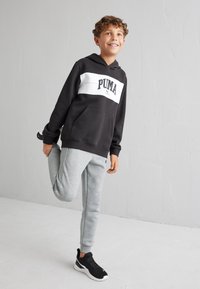 Sudadera PUMA en blanco y negro con bolsillo delantero, combinada con pantalones de chándal grises y zapatillas negras, diseñada para la comodidad y la movilidad.