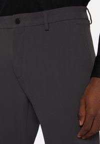 Grijze broek van gladde stof, met een metalen knoop, riemlussen en een slim fit ontwerp met zakken aan de zijkanten.