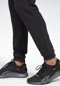 Black athletic shoes with gray accents, featuring a textured sole and mesh upper. Slim-fit black sweatpants with ribbed cuffs.