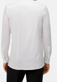 Chemise blanche à manches longues avec une coupe droite, des poignets boutonnés et une texture lisse. Elle présente un col classique et aucun motif ni logo visible.