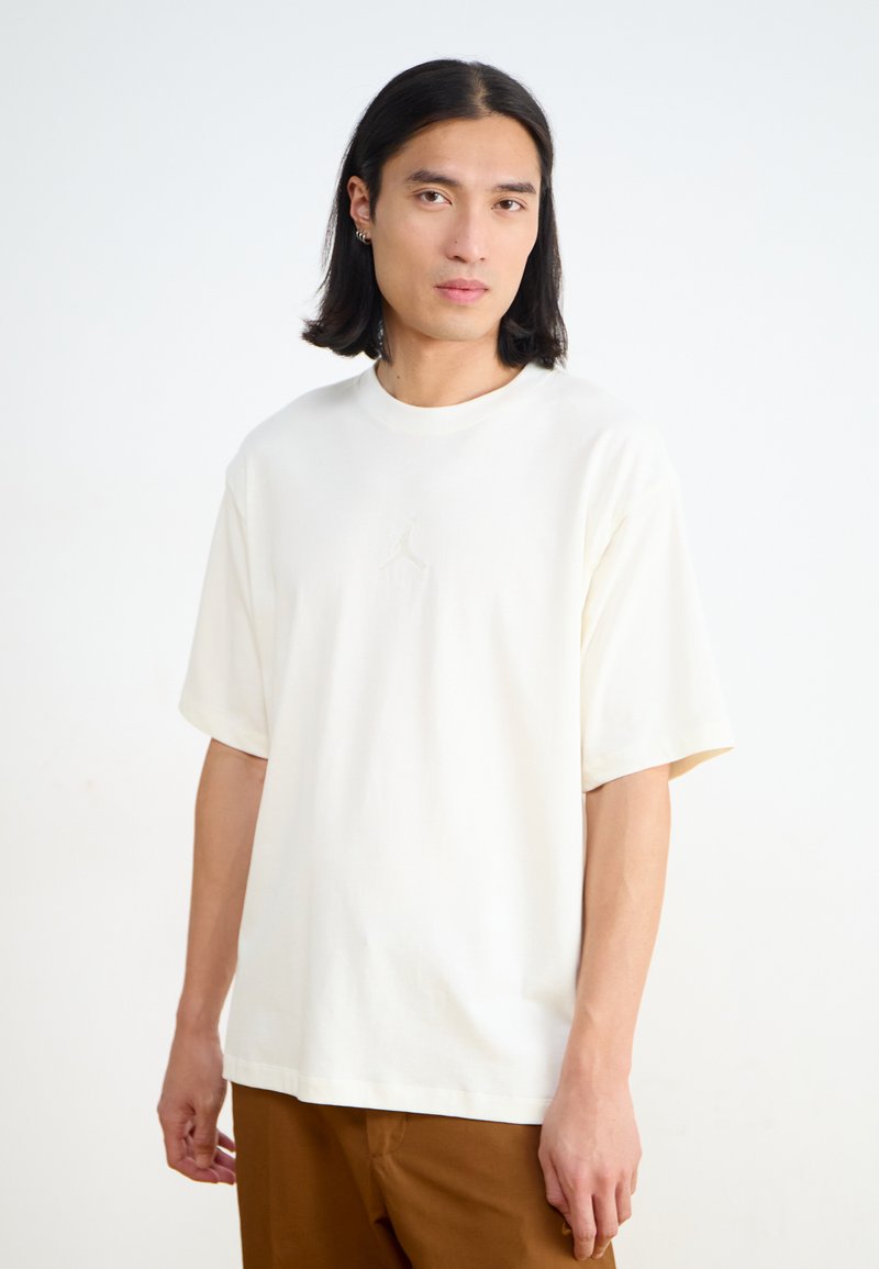 Creme-kleurig katoenen t-shirt met korte mouwen, voorzien van een subtiel reliëflogo nabij het midden. Eenvoudig, relaxte pasvorm.