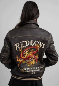 Veste bomber en cuir marron, avec un motif de dragon brodé et le texte "REDSKINS" au dos, dotée de poignets et d'un ourlet côtelés.