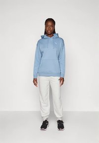 Hanorac bleu deschis cu glugă, buzunar tip cangur și șnur de ajustare; asortat cu pantaloni de trening gri și pantofi sport negri cu accente roz.