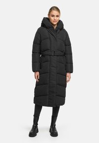 Long black puffer coat, quilted design with a belt, oversized hood, front zip, and side pockets. Textured fabric with a matte finish.
