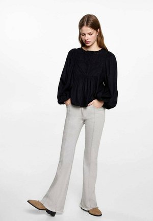 Blusa nera in cotone con maniche a sbuffo e dettagli in pizzo, abbinata a jeans grigi chiari a campana con orli sfilacciati e una texture liscia.