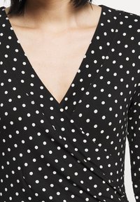 Mustaha musta, jossa valkoisia pilkkuja, V-pääntie, pitkät hihat ja sileä kangas. Sopii erilaisiin tilaisuuksiin.