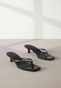 Infradito aperti neri in pelle con forma quadrata, sottili fasce incrociate e tacco a blocco piccolo, caratterizzati da una superficie liscia.