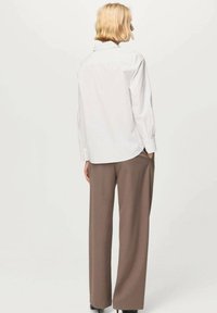 Biela košeľa na gombíky s oblým lemom a dlhými rukávmi, kombinovaná s voľnými hnedými nohavicami a čiernymi topánkami. Hladká textúra, klasický dizajn.