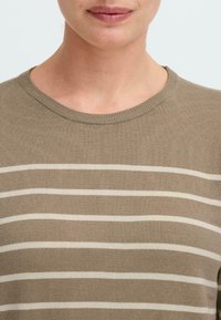 Beige Strickpullover mit weißen horizontalen Streifen, Rundhalsausschnitt und Rippstrickabschlüssen. Weiche Textur und lässiges Design. Nahaufnahme.