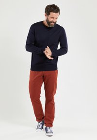 Marineblauwe langwerpige trui, oranje broek en blauwe sneakers. Casual pasvorm met ribbelmanchetten en -zoom. Eenvoudig ontwerp, geen patronen of accenten.
