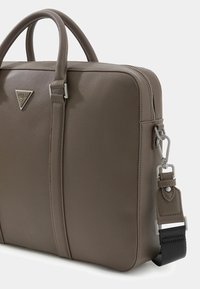 Brown faux leather laptop bag with dual handles, zip closure, silver logo plaque, and detachable shoulder strap featuring black fabric detailing.