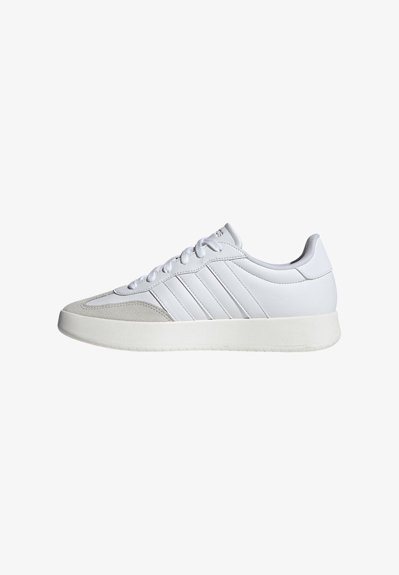 Zapatos deportivos blancos con parte superior sintética lisa, detalles de ante gris claro, seis ojales y suela de goma blanca texturizada.