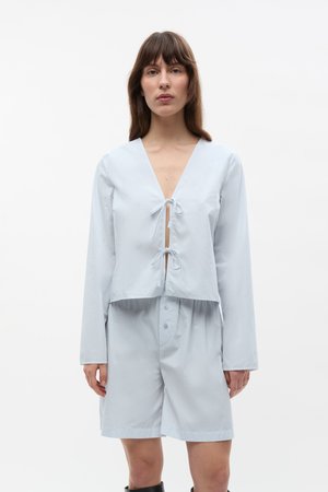 Lichtblauw twee-delig outfit met een cropped top met V-hals en strikdetail, gecombineerd met bijpassende shorts en subtiele knoopaccenten.