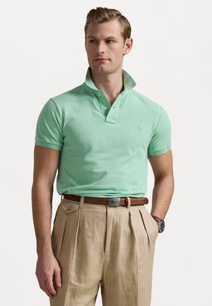 Lichtgroene polo met een klassieke kraag en een twee-knops sluiting, gecombineerd met beige geplooide broek en een brown leren riem.