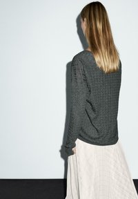 Dunkelgrauer Strickpullover mit einem strukturierten Muster, kombiniert mit einem leichten, fließenden Rock, der diagonale Steppungen aufweist. Rückansicht des Outfits.