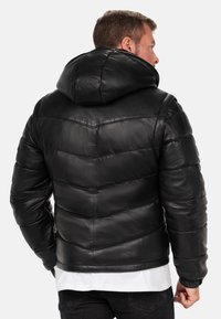 Zwarte leren pufferjack met een capuchon, gewatteerde textuur, contrasterende stiksels en elastische manchetten. Heeft een getailleerd ontwerp en een eenvoudige kraag.