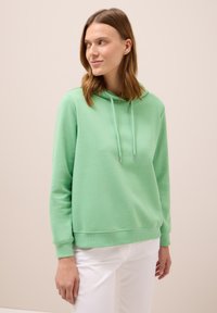 Felpa verde menta realizzata in tessuto morbido. Presenta un cappuccio con cordini, polsini a costine e orlo a costine. Abbinata a pantaloni bianchi. Design semplice.
