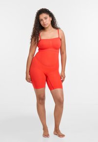 Červený bodysuit ze tvarovacího materiálu s nastavitelými ramínky, délka do poloviny stehna, hladká textura a bezešvé provedení. Má podporující a strukturovaný dekolt.