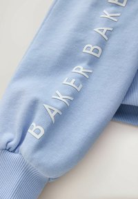Tissu de sweat-shirt bleu clair avec poignets côtes, comportant un texte blanc en relief "BAKER" le long de la manche. Texture lisse, design décontracté.