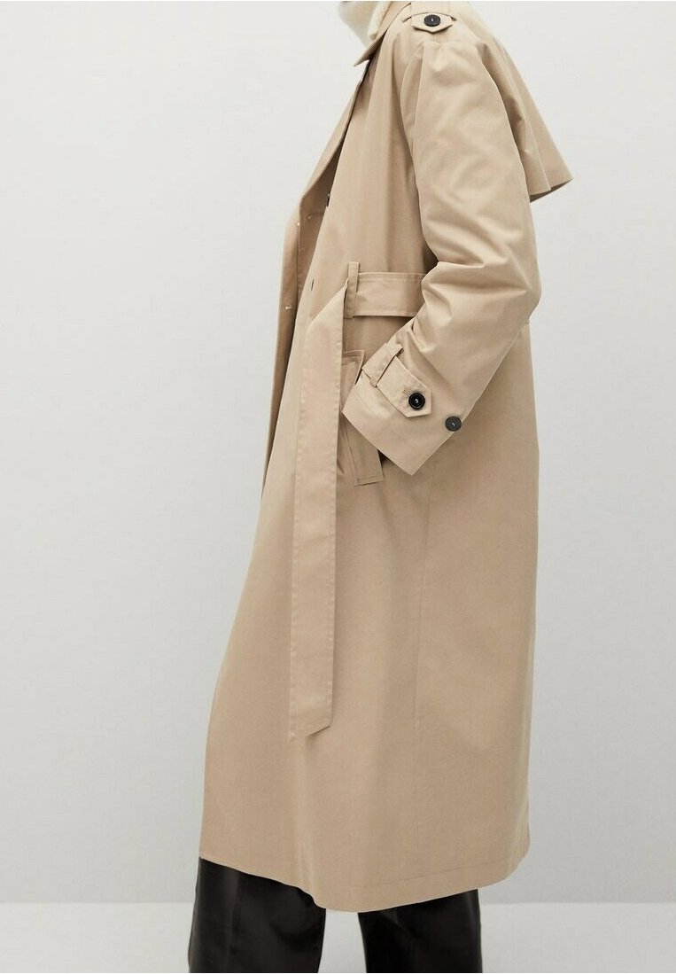 Beżowy trencz z paskiem w talii, z guzikami na mankietach i epoletami. Wykonany z gładkiego materiału, o prostym kroju, sięgającym do połowy łydki.