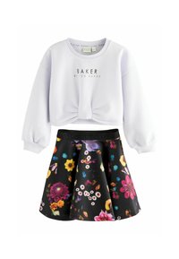 Sweatshirt blanc court avec le texte "BAKER", associé à une jupe noire évasée ornée de motifs floraux vibrants dans diverses couleurs.