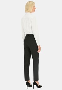 Biała koszula z guzikami, dopasowany krój, długie rękawy; zestawiona z dopasowanymi, teksturowanymi ciemnymi spodniami i czarnymi szpilkami.