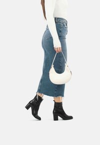Sac hobo blanc avec détails en argent, jupe midi en denim avec ourlet effiloché, bottines à talons noires, portées avec un top ajusté à manches longues.