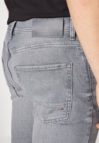 Vaqueros de mezclilla grises con un parche trasero con el logotipo "TOMMY HILFIGER", detalles de costura sutiles y un pequeño acento de bandera en el bolsillo.