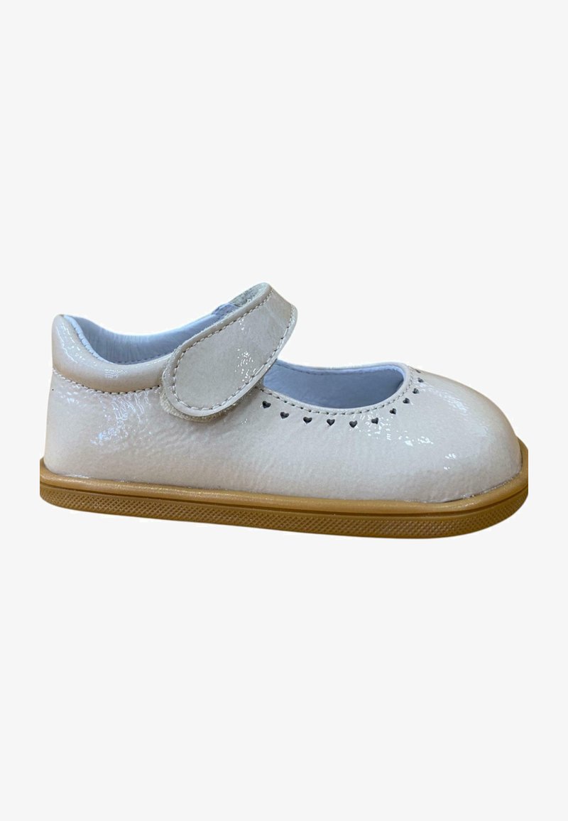 Zapato Mary Jane de charol blanco con punta redonda, correa de velcro y pequeños cortes en forma de corazón a lo largo del borde. Suela de goma de color marrón.