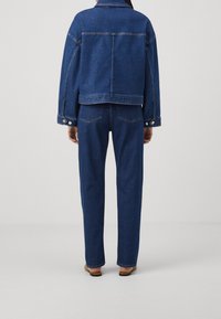 Siniset farkkutakki ja siihen sopivat housut, molemmissa rento istuvuus, näkyvät sauma- ja ompeludetaljit sekä tavalliset metalliosat.