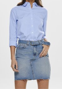 Chemise à rayures bleu clair avec des manches retroussées, associée à une jupe en denim clair avec une coupe effilochée et une ceinture assortie.