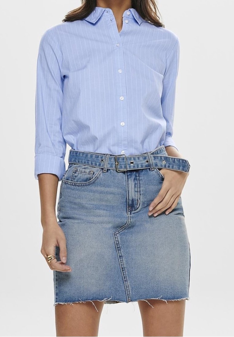 Chemise à rayures bleu clair avec des manches retroussées, associée à une jupe en denim clair avec une coupe effilochée et une ceinture assortie.