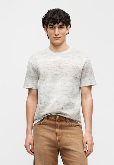 Ανοιχτό γκρι κοντομάνικο t-shirt με ανάγλυφο ζιγκ-ζαγκ σχέδιο, λαιμόκοψη crew και άνετη εφαρμογή, σε συνδυασμό με τζιν παντελόνι από ανοιχτό καφέ ντένιμ.