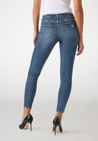 Jeans ajustados de mezclilla azul oscuro, con una cintura alta, dos bolsillos traseros y detalles de costura sutiles. Combinados con tacones negros altos.