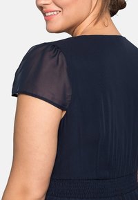 Robe marine avec des manches courtes transparentes, une taille smockée et une texture lisse, présentant une silhouette classique et des lignes de design épurées.