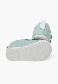 Scarpa verde menta con texture liscia, suola in gomma bianca e cinturini in Velcro regolabili. Presenta un tallone imbottito per il supporto.