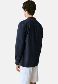 Tmavomodrá košeľa s dlhým rukávom vyrobená z mäkkej tkaniny, s golierom na gombíky a gombíkovými manžetami, zobrazená zozadu.