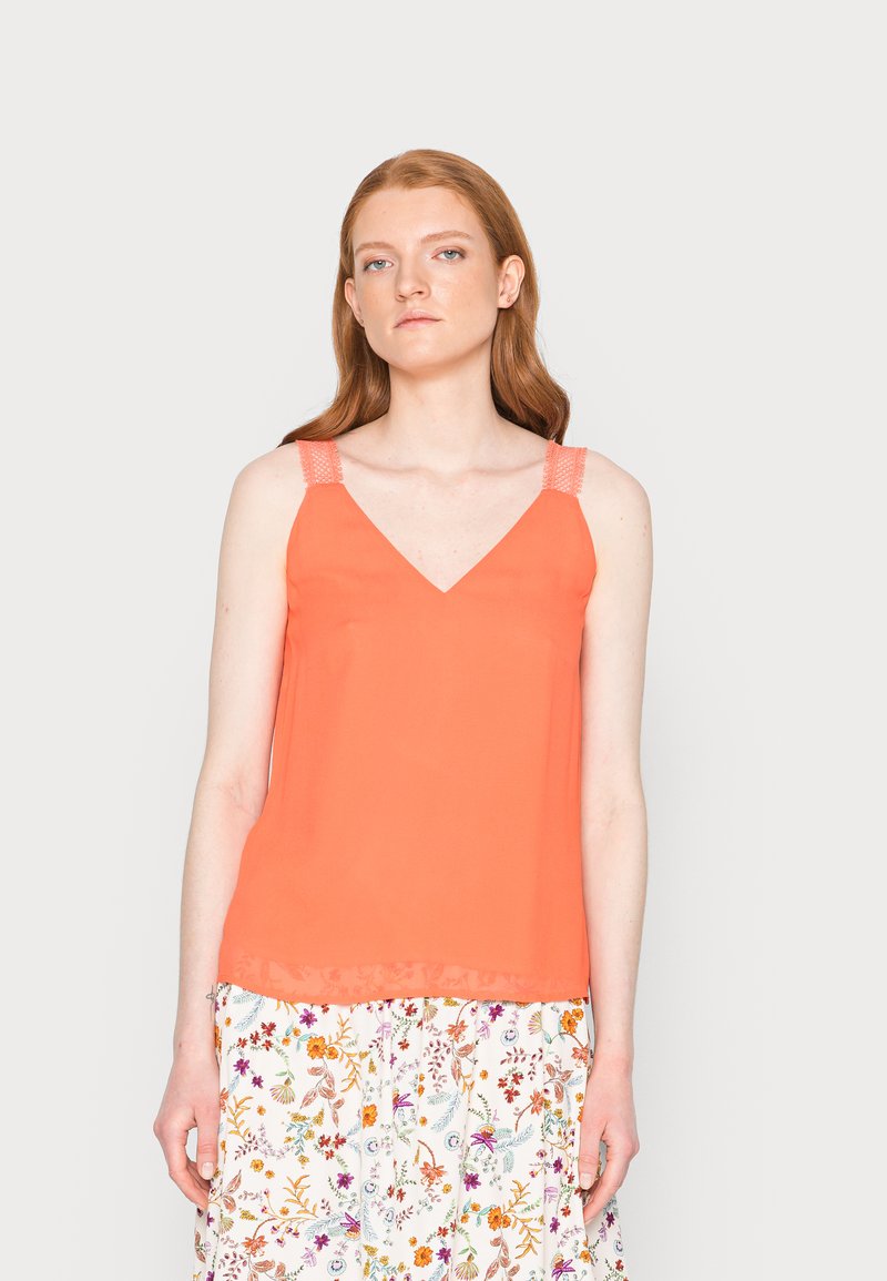 Top sem mangas corais com decote em V, apresentando alças de malha e um design fluido. Combinado com uma saia com padrão floral.