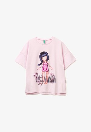 Chemise rose clair à manches courtes avec une illustration d'une fille portant une tenue rose, aux longs cheveux foncés, debout parmi l'herbe, les fleurs et un animal en peluche.