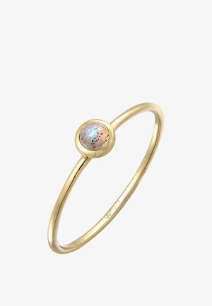 Guld ring med en rund, multifarvet sten med sorte prikker. Selve bæltet er glat og slankt, hvilket fremhæver et minimalistisk design.