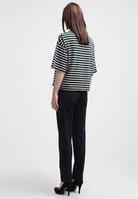 Top a righe a maniche corte di colore verde scuro e bianco, abbinato a pantaloni blu navy. Il top ha una vestibilità ampia e maniche larghe.Tacchi neri completano il look.