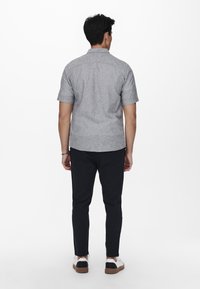 Camisa de manga corta gris con botones, de tela ligera, textura suave, combinada con pantalones negros ajustados y zapatillas blancas con detalles negros.