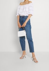 Bílý top na jedno rameno s výřezy, doplněný vysokými modrými džíny, bílou kabelkou se zlatým řetízkem a bílými sandály na podpatku.