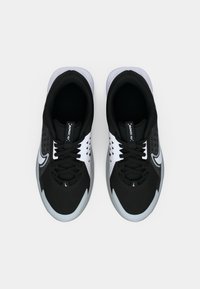 Fekete sportcipők texturált felső résszel, fehér akcentussal és szürke talppal. Zsinóros kialakításúak, és oldalt logóval rendelkeznek.