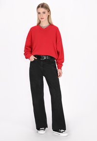 Felpa rossa oversize con spalle scese, pantaloni neri a gamba larga e sneakers bianco e nere. Tessuti morbidi e vestibilità casual.