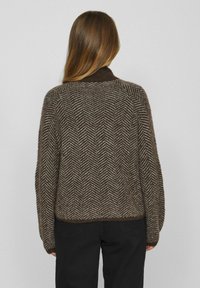 Maglione marrone a motivo spigato con colletto alto, vestibilità ampia e orlo a coste. Realizzato in materiale a maglia testurizzata, con maniche lunghe.