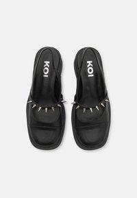 Pantofi slip-on negri, cu o textură de piele netedă, o formă unghiulară și ținte decorative argintii pe partea din față. Logo imprimat pe tălpile interioare.