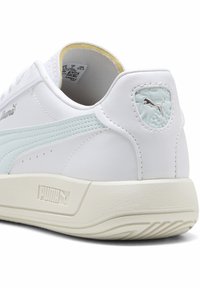 Hvid Puma sneaker med lyseblå striber, struktureret sål og Puma-logo på hælen og midtsole, set fra bagsiden.