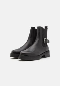 Bottines en cuir noir avec une finition lisse, bout rond, talon bloc, panneaux latéraux élastiques et un accent décoratif de boucle en argent.